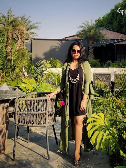 A black dress with a long olive green shrug and a statement necklace, perfect for a garden cafe.
