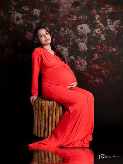 A powerful and artistic portrait of a mom-to-be in a red gown. The dark floral backdrop and water reflection effect create a moody and dramatic look.