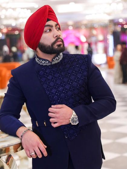 A client looking sharp in a custom navy blue Indo-Western jacket. The piece features an asymmetrical design with a textured, embellished panel and a decorated collar.