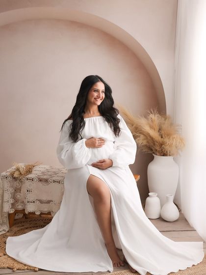 The flowing white gown and the soft, natural light create an angelic and timeless feel in this solo maternity portrait.