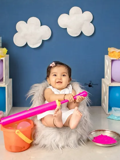 A sweet baby girl ready for her first Holi, sitting comfortably in our fluffy chair with her colorful props.