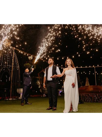 A grand entrance with sparklers. The bride's modern white gown and the groom's sharp waistcoat create a stunning visual for their evening celebration.