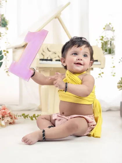 Holding up her number one. This bright and cheerful studio setup with a miniature piano is perfect for a first birthday celebration.
