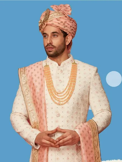 We believe every groom deserves to feel like royalty. This classic ivory sherwani with intricate embroidery, paired with a pastel pink safa and dupatta, is a timeless choice for a regal wedding look.