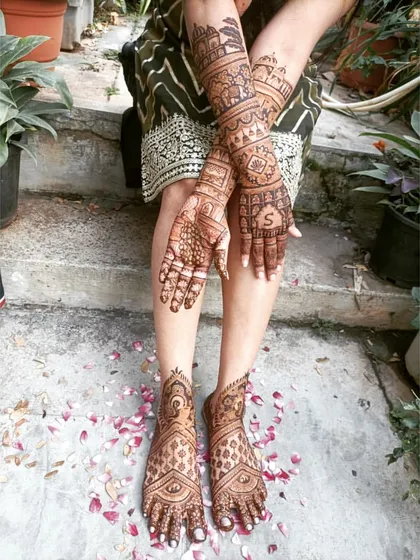 A full view of a bride sitting with her hands and feet adorned with my mehendi, showcasing the complete, cohesive artwork.