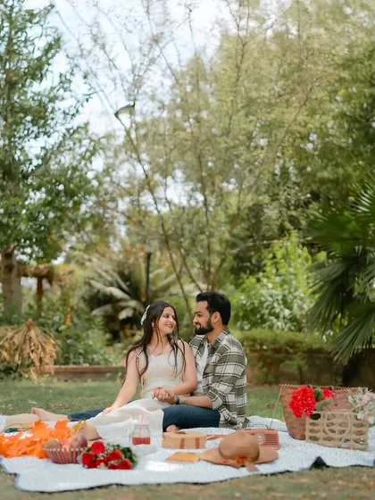 A beautiful wide shot of the picnic setup, showing the couple enjoying a quiet moment in a lush garden setting.