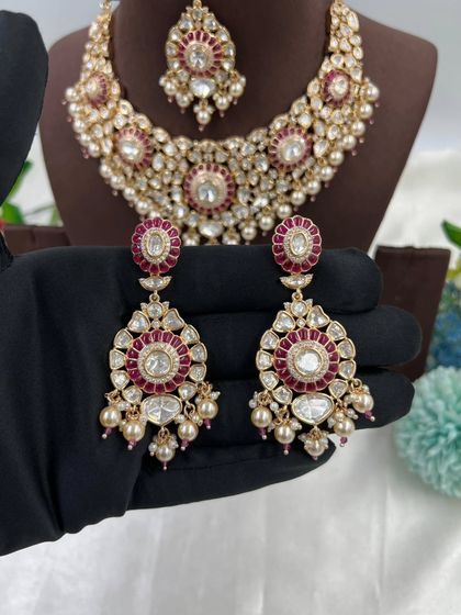 The Zarista Premium Moissanite Necklace set, shown here in both ruby and green variations. This set includes a necklace, maang tikka, and earrings, featuring large central stones surrounded by detailed craftsmanship.