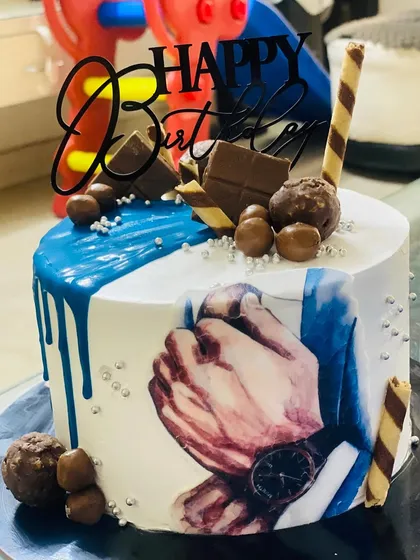 A stylish men's birthday cake with a blue drip and chocolate decorations.