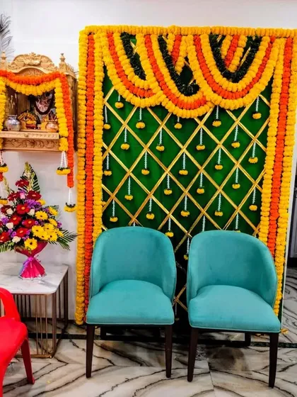 A vibrant setup for a house pooja in Vile Parle. We created a backdrop with orange and yellow marigold garlands against a green panel, perfectly complementing the small wooden home mandir.