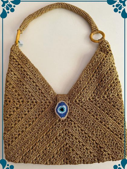 This mustard shoulder bag features a unique V-shape design and a central Evil Eye charm. It's a versatile piece that adds a pop of color and personality to any outfit.