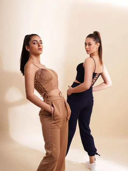 Two models styled in contemporary bustier tops and trousers. This shot showcases trendy designs with details like corset lacing, appealing to a youthful market.