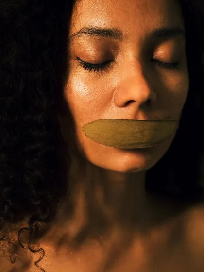 A conceptual fine art portrait titled "The Melody of Stillness." A dried leaf placed over the mouth suggests silence and a connection to nature, creating a poetic and thought-provoking image.