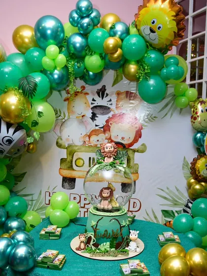 The full jungle theme setup, complete with a custom cake table, animal balloons, and a lush green backdrop.