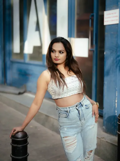 A relaxed street portrait with a beautiful blue background. The soft, natural light and the model's casual pose create a fresh and effortless fashion shot.