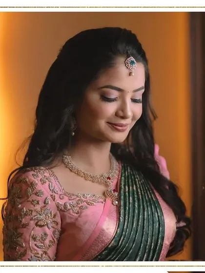 A portrait of soft elegance. The makeup is subtle and romantic, with a soft pink lip and gentle shimmer on the eyes, perfectly complementing her pink and green saree.