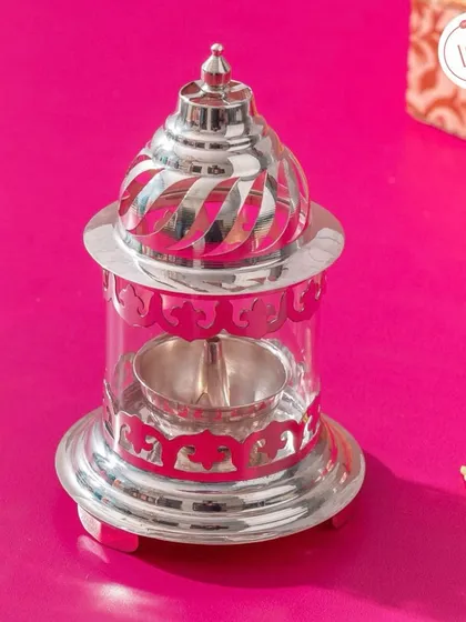 A stunning pure silver akhand diya (covered lamp) with intricate jaali work. This is a luxurious and traditional gift that will be cherished for years.