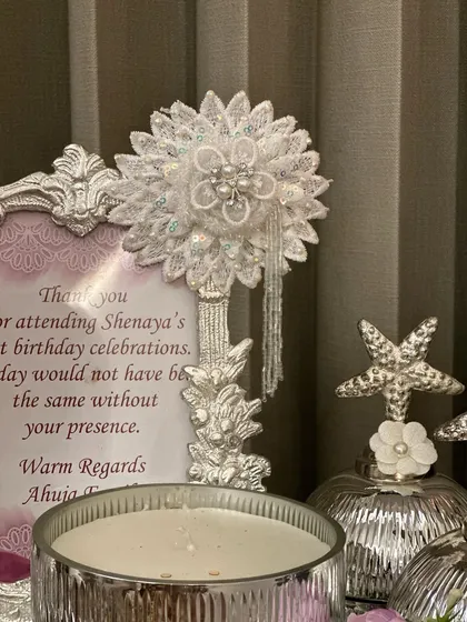 A close-up of a personalized thank you note from a first birthday celebration, paired with a delicate, handcrafted floral stick.