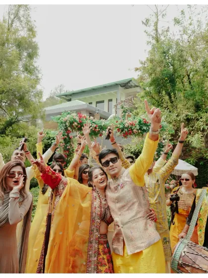 A candid group photo of the couple with their friends, all raising their hands in celebration during the Haldi entry.
