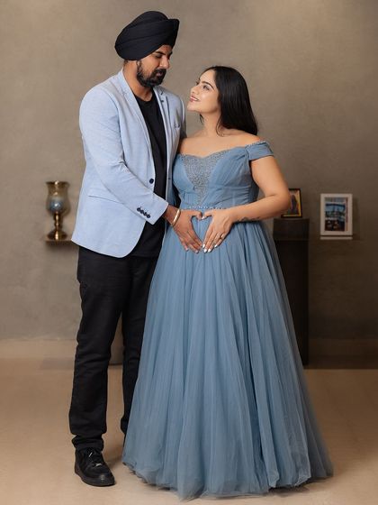 A classic portrait of the expecting couple. The mother-to-be makes a heart shape with her hands on her belly, a sweet and timeless gesture of love for their coming baby.