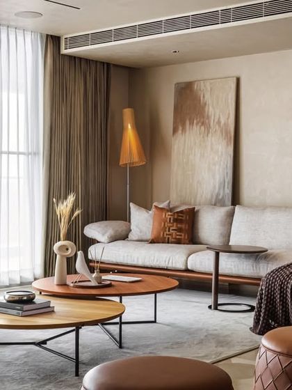 The living room of the apartment embodies quiet luxury with its monochromatic color palette and clean lines. A comfortable sofa, elegant armchair, and layered coffee tables create a refined and understated space for relaxation.