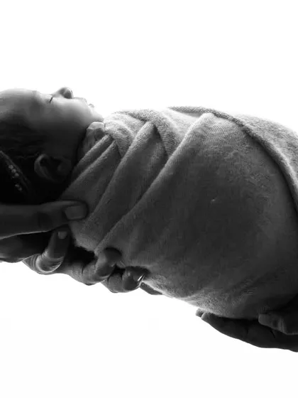 Sometimes, the simplest images are the most powerful. This black and white photograph of a newborn held safely in their parents' hands symbolizes the beginning of a new life and a family's love. It's a very artistic and minimalist newborn shot.