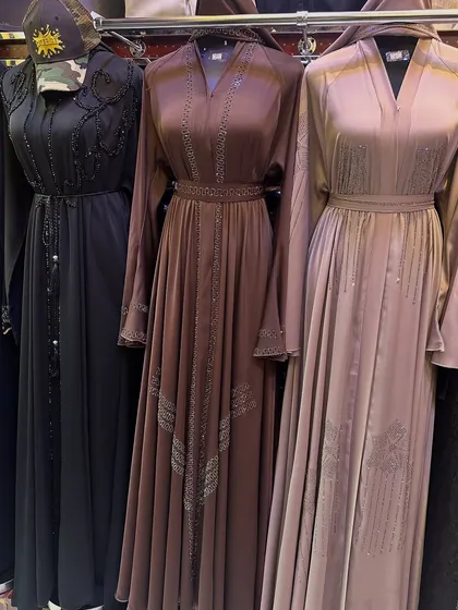 Showcasing abayas in rich brown and champagne tones with delicate beading. The V-neck cut and belted waist create a flattering silhouette for these elegant garments.