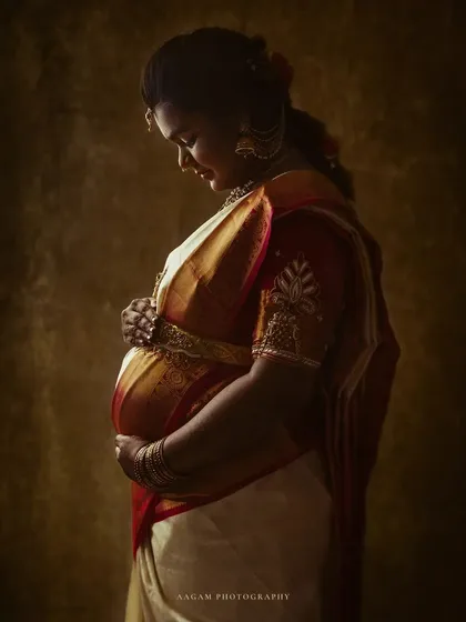 A quiet, contemplative portrait of a mother-to-be in a traditional silk saree. The lighting is soft and painterly, honoring her heritage with grace.