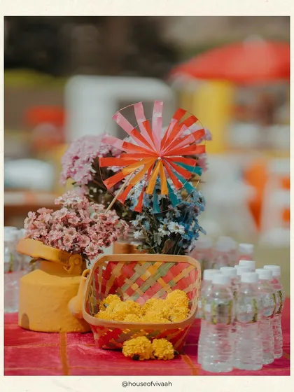 A close-up of a table at the Kite Carnival, with a colorful pinwheel, marigolds in a woven basket, and other small details that contribute to the festive, mela-like atmosphere.