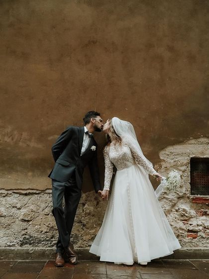 A tender kiss against a textured wall, capturing a moment of private affection during their public celebration.