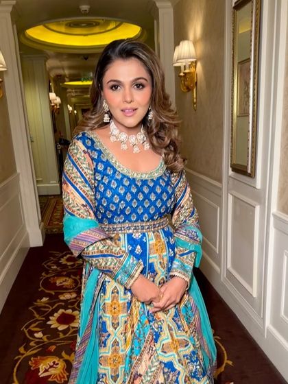 A full-length shot of the beautiful blue and gold anarkali. The makeup is designed to complement the rich colors of the outfit, with a focus on warm tones and a radiant finish.