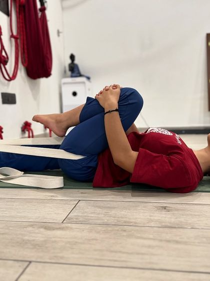 This is Supta Eka Pada Pavanamuktasana, where a belt is used to create traction. The belt around the foot of the straight leg helps to ground the femur, allowing for a deeper and more stable release in the hip of the bent leg.