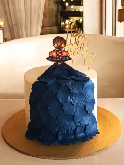 An artistic and fashionable cake featuring a topper of a girl in a flowing blue gown created with textured buttercream petals.