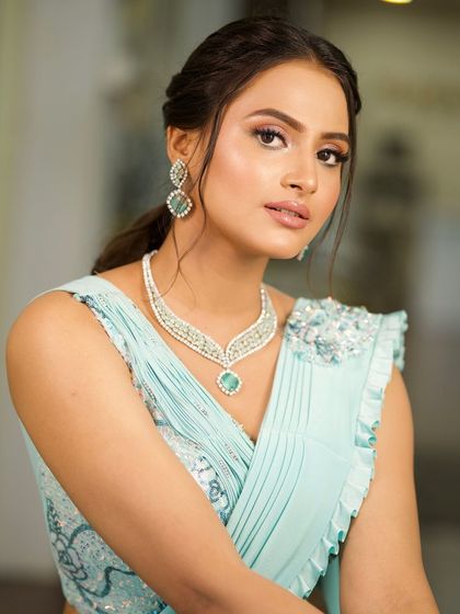 A close-up of a client in a light blue saree, showcasing her diamond and emerald jewelry and the soft, elegant makeup.