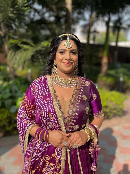 A full-length shot showcasing her beautiful purple lehenga. The makeup is designed to complement the rich colors without overpowering them.