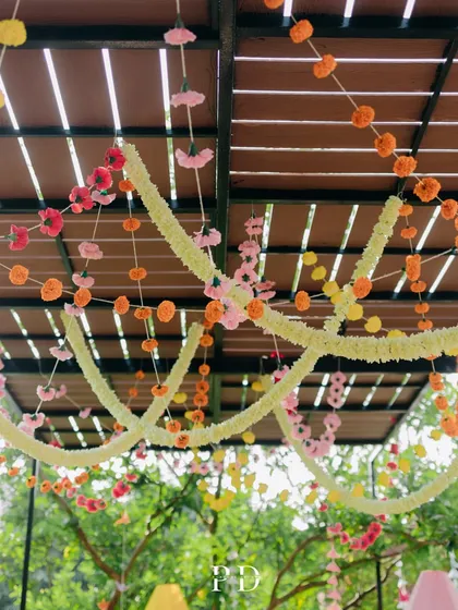 A ceiling of colorful marigold and tuberose garlands, creating a festive and traditional canopy for a Mehendi ceremony.