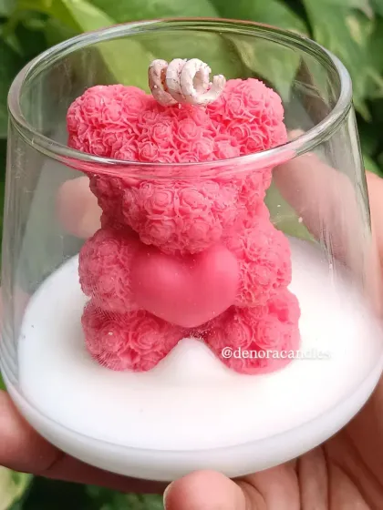 The pink teddy bear jar candle held against a leafy background.
