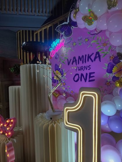 A detailed shot of the 'VAMIKA turns ONE' text on the custom backdrop, with the 'Happy Birthday' neon sign and light-up '1' adding a warm glow.