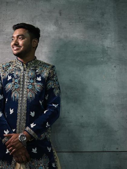 A client looking sharp against a modern backdrop in our royal blue velvet sherwani. The intricate silver and blue embroidery creates a stunning, artistic effect.