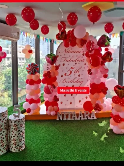 A sweet strawberry-themed 5th birthday. The red, pink, and white decor includes a custom backdrop, strawberry and candy-shaped balloons, and themed plinths.