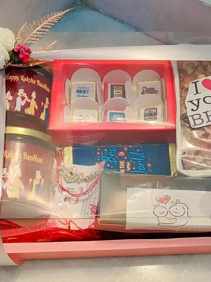 A premium Rakhi hamper in a tray, containing jars with custom labels, a "Brother of the World" chocolate bar, and a box of personalized chocolates.