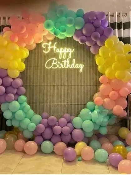 A vibrant pastel rainbow balloon arch with a 'Happy Birthday' neon sign, creating a perfect photo backdrop.