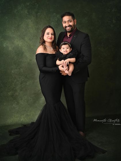 An elegant and formal family portrait. The mother's flowing black gown and the father's sharp suit create a sophisticated look, while their baby girl's smile adds the perfect touch of sweetness.