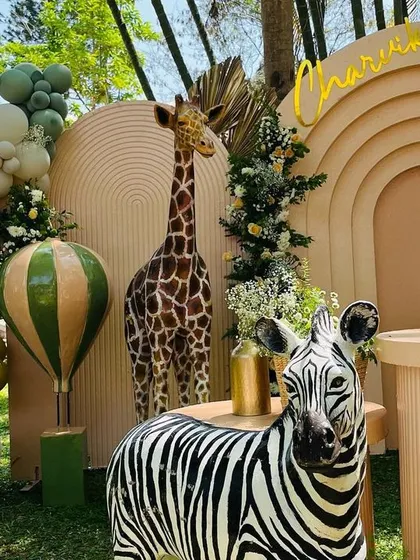 A chic and modern safari theme for Charvik's party. This setup uses a neutral color palette with pops of green and yellow, featuring a corrugated backdrop, a tall giraffe, a zebra, and a hot air balloon prop for a stylish take on the jungle.