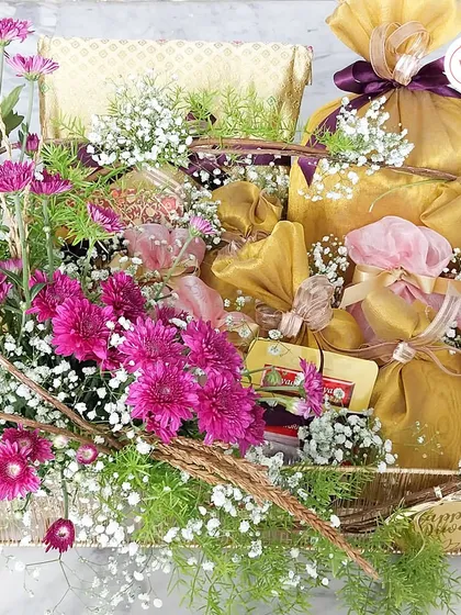 A larger view of the festive dry fruit hamper, showing the gold-wrapped potlis and other goodies nestled among the flowers.