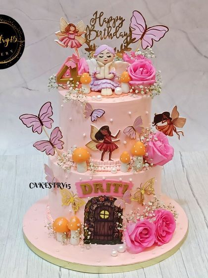 A magical two-tiered pineapple cake with a fairy theme. The cake is adorned with a fondant fairy, an edible fairy picture, real roses, and whimsical mushrooms.