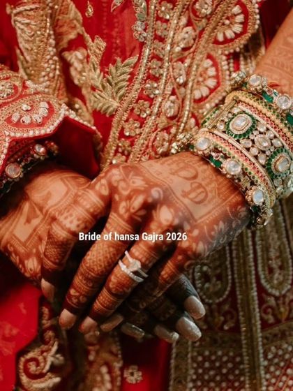 A close-up of the bride's hands, showcasing the intricate mehendi against her rich red lehenga. The detail on her bangles and the henna work is simply stunning.