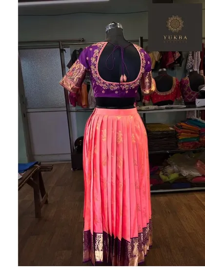 The back view of the purple and pink lehenga set, highlighting the embroidered back of the blouse and the flow of the pleated skirt.