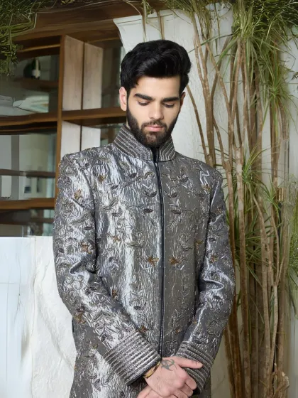 A masterpiece in gunmetal silk, this sherwani is elevated with intricate all-over threadwork. The sculpted shoulders and textural cuffs create a powerful blend of regality and modern edge, perfect for a groom or for making a statement at a grand event.