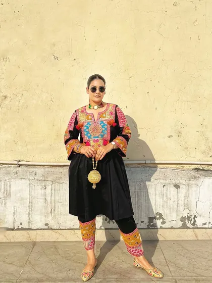 I love how the sunlight catches the texture of this handcrafted golden potli, highlighting its spherical shape and delicate details against the dark, embroidered outfit.
