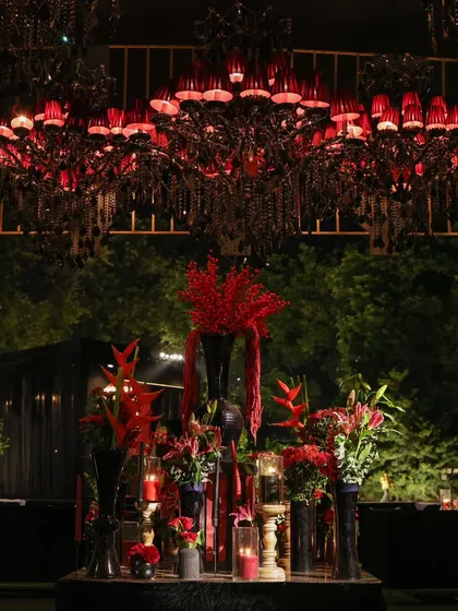 A dramatic focal point featuring a stunning red-shaded chandelier above a curated arrangement of red florals and decor elements, perfectly capturing the event's bold aesthetic.